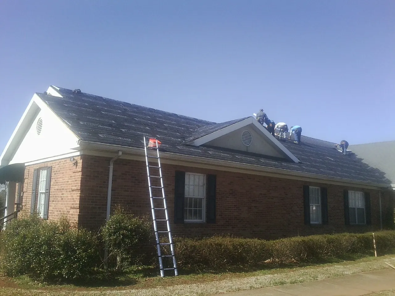 Crew tearing shingles off a brick ranch roof with a ladder set — Emergency Roof Repair work by our crew in White Plains