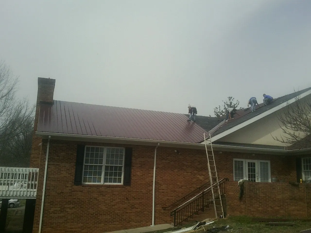 Crew setting red metal roofing panels on a brick home in White Plains