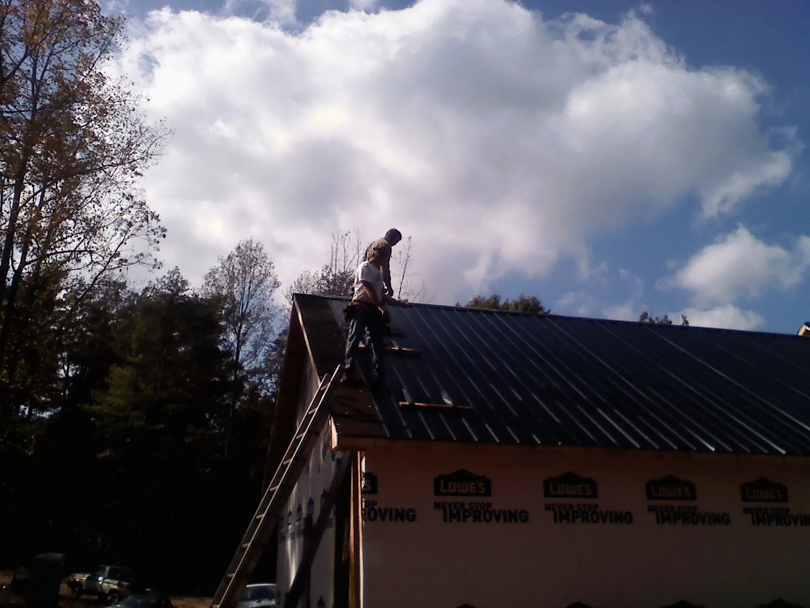 Roofer fastening dark metal panels high against a cloudy sky, from a Roof Inspection job in White Plains